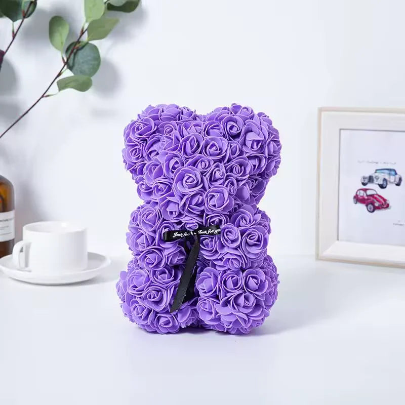 Ursinho de rosas roxas com laço preto ao lado de xícara e quadro