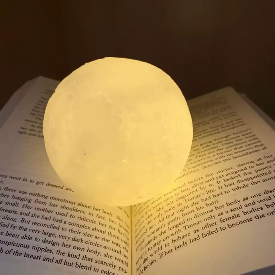 Luminária lua acesa sobre livro aberto, iluminando o ambiente